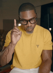 a man wearing glasses and a yellow t-shirt with a prada logo on it