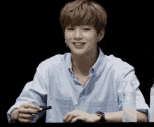 a young man in a blue shirt is smiling and holding a marker