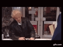 a woman in a black leather jacket is sitting at a table in front of a store .