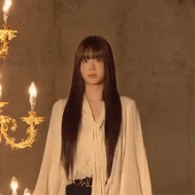 a woman with long hair is standing in front of a chandelier and candles .