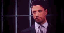 a man in a suit and tie is standing in front of a window with a red light behind him .