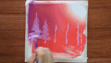 a person is painting a picture of trees on a red and purple background