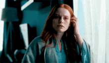 a woman with red hair is standing in front of a window and touching her hair