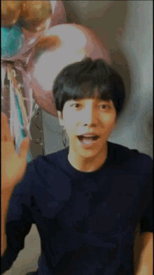 a young man in a blue shirt is waving in front of balloons