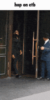a man in a suit is walking out of a door with the words hop on etb above him