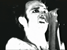 a man without a shirt is singing into a microphone .