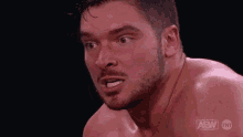 a shirtless wrestler with a beard is making a funny face in a wrestling match .