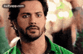 a man with a beard wearing a green shirt is looking at the camera .