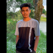 a young man stands in front of a tree wearing a black and white shirt