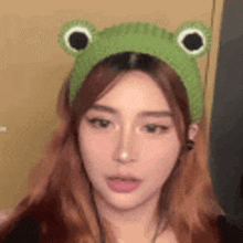 a woman is wearing a green frog headband and headphones .