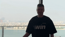 a man wearing a shirt that says win is standing in front of a window