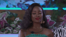 a woman wearing a green top and gold earrings is sitting in front of flowers