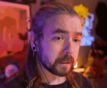 a man with long hair and a beard is wearing headphones and making a surprised face .