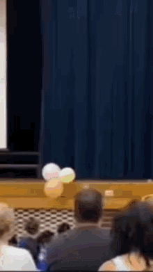 a group of people are sitting in front of a stage with balloons in the air .