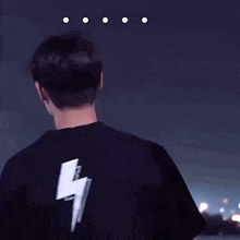 a man in a black shirt is standing in front of a city at night with his hand in the air .