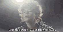 a man singing into a microphone with the words " looking down at all of the wreckage " below him