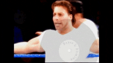 a man wearing a white shirt with the word wrestling on it is in a boxing ring