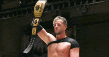 a wrestler is holding a wrestling belt in his hand .