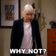 a woman in a suit says " why not " while standing in front of a dresser
