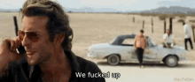 a man is talking on a cell phone in front of a car and says we fucked up .
