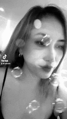 a black and white photo of a woman blowing soap bubbles in front of her face .