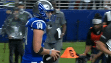 a football player with the number 14 on his jersey is holding a football .