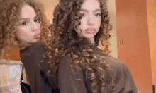 two girls with curly hair are standing next to each other and posing for a picture .