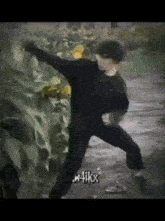 a man in a black shirt and black pants is standing in front of a bush with the words kuwa41kx on the bottom