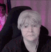 a man wearing glasses and a wig is sitting in a chair and looking at the camera .
