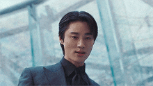 a young man wearing a suit and tie is standing in front of a glass building .