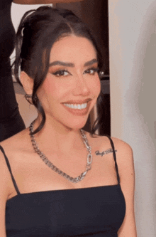 a woman wearing a black top and a chain necklace smiles for the camera