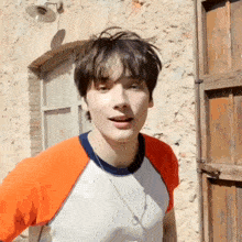 a young man wearing an orange and white shirt is standing in front of a stone wall .