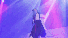 a woman singing into a microphone with her arms outstretched in front of a purple background