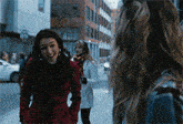 a woman in a red coat is talking to another woman on a sidewalk
