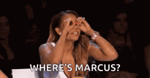 a woman is sitting in front of a crowd and covering her eyes with her hands while asking where 's marcus .