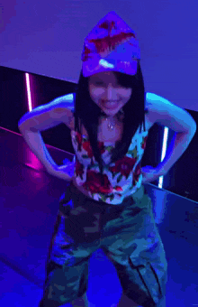 a girl wearing a hat and a floral top is standing with her hands on her hips