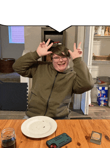 a boy sitting at a table with a phone and a plate
