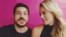 a man and a woman are looking at each other and smiling in front of a pink background .