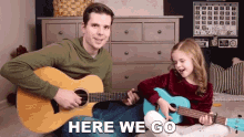 a man is playing a guitar and a little girl is playing a ukulele with the words here we go behind them