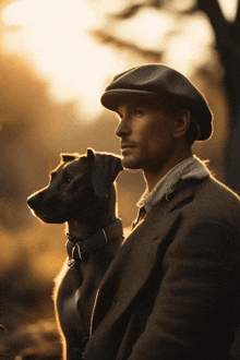 a man in a hat holds a black dog on his shoulder