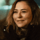 a woman wearing a black jacket and a grey sweater smiles for the camera