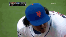 a baseball player wearing a blue ny mets hat looks down at something