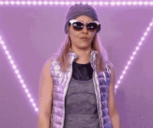 a woman wearing a hat and sunglasses is standing in front of a purple background .