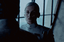 a woman in a white uniform is standing next to a man in a dark room looking at him .