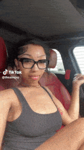 a woman wearing glasses is sitting in the driver 's seat of a car with tiktok at the bottom