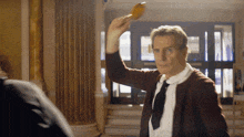 a man in a brown cardigan and tie is holding a yellow object in his hand