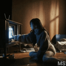 a woman is sitting on the floor looking at a television with the letters ms behind her