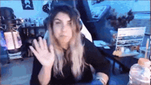 a woman is waving her hand while sitting in front of a computer monitor .