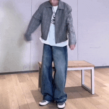 a man wearing a grey jacket and blue jeans is standing next to a small table .