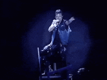 a man is singing into a microphone while sitting in a chair on a stage .